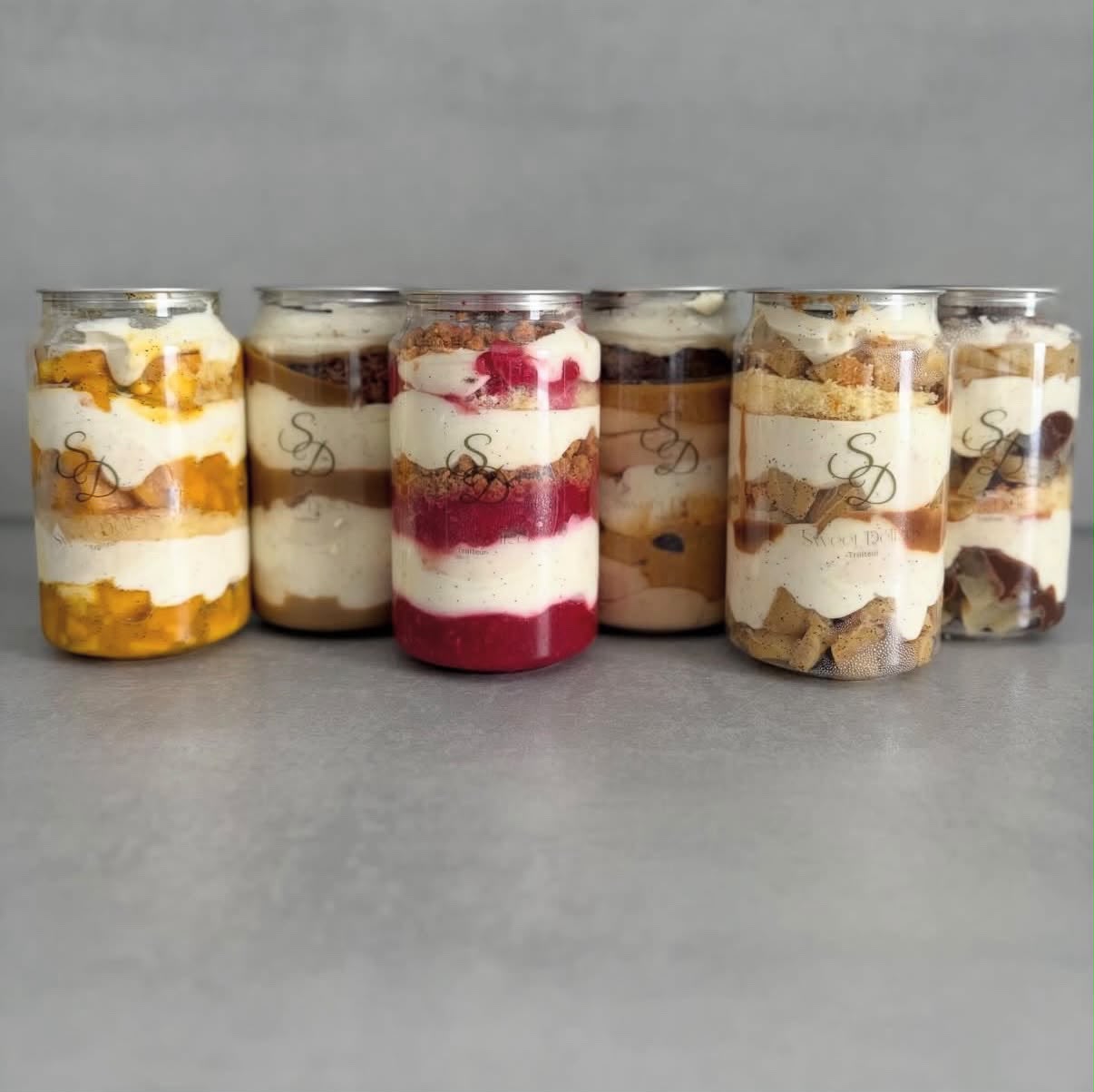 Six canette cakes alignés : mangue, caramel, fruits rouges, chocolat, pomme et poire